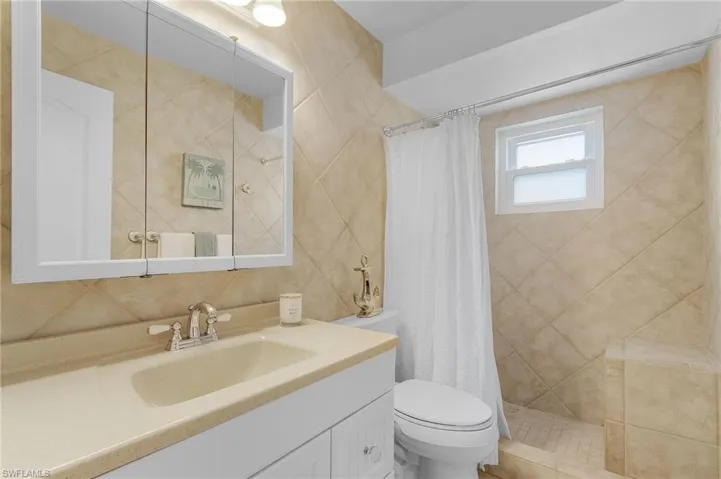 Bathroom with vanity, backsplash, a shower with shower curtain, toilet, and tile walls