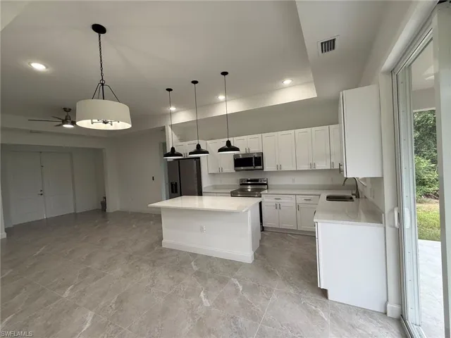 Kitchen with pendant lighting, a kitchen island, appliances with stainless steel finishes, white cabinetry, and light stone countertops