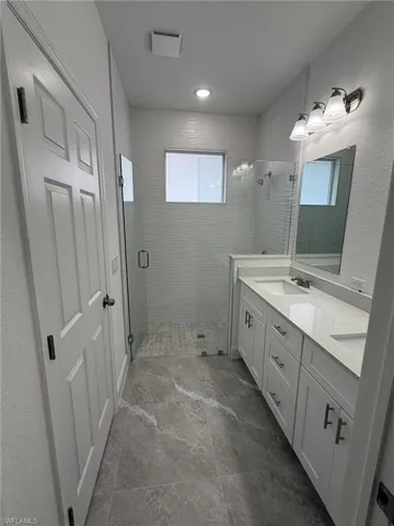 Full bath with double vanity, a stall shower, and a textured wall
