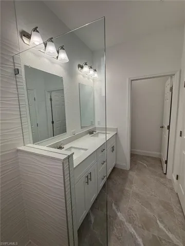 Bathroom with double vanity, walk in shower, and a textured wall