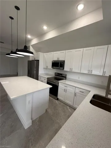 Kitchen with stainless steel appliances, white cabinets, light stone countertops, a center island, and recessed lighting