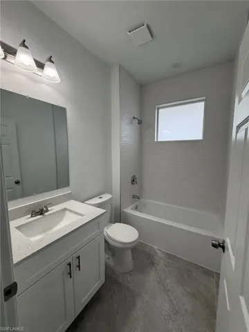 Bathroom with shower / washtub combination, vanity, and a textured wall