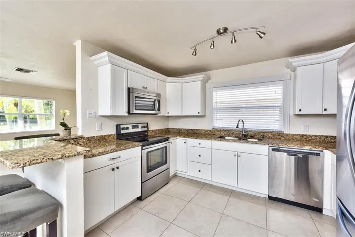 Kitchen featuring dark stone countertops, visible vents, light tile patterned flooring, a sink, and stainless steel appliances