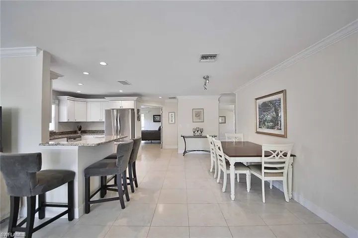 Kitchen with light tile patterned floors, visible vents, a peninsula, a kitchen bar, and crown molding
