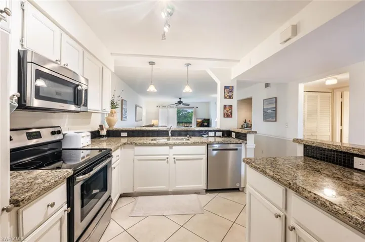 Kitchen with stainless steel appliances, white cabinetry, dark stone counters, ceiling fan, and a peninsula