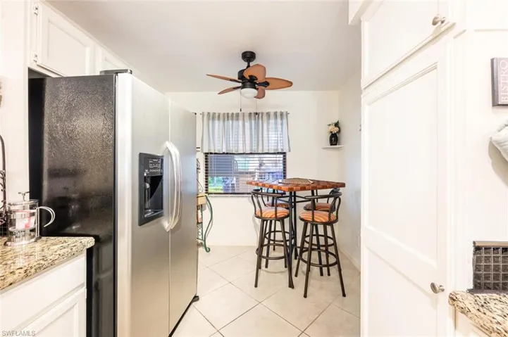 Kitchen featuring white cabinets, stainless steel refrigerator with ice dispenser, light stone countertops, light tile patterned floors, and a ceiling fan