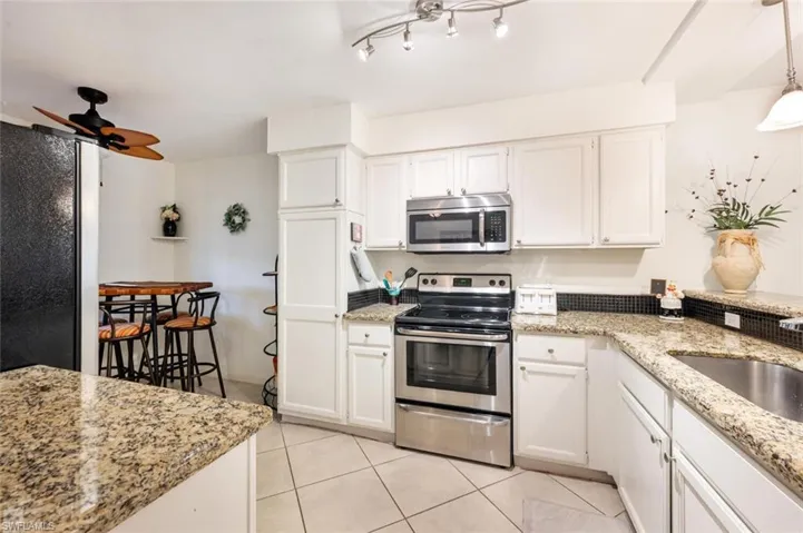 Kitchen featuring stainless steel appliances, light tile patterned floors, white cabinets, and light stone counters