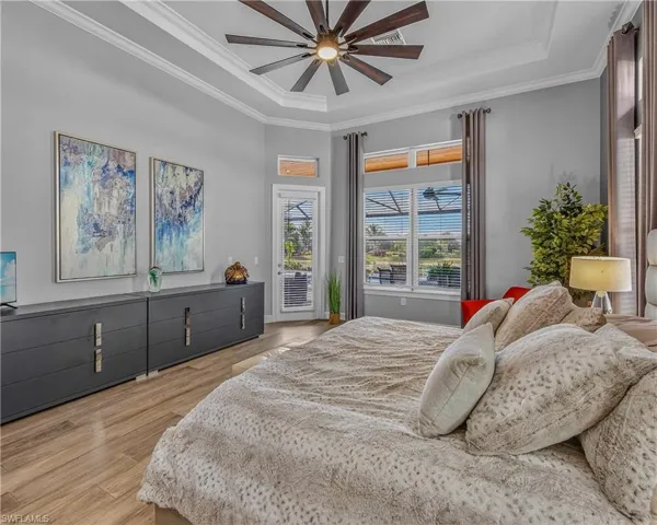 Bedroom with access to exterior, a raised ceiling, ceiling fan, ornamental molding, and light wood-type flooring