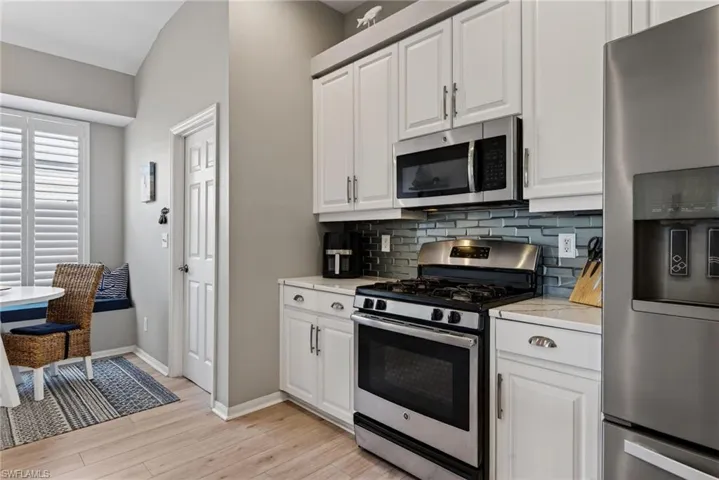Kitchen featuring stainless steel appliances, white cabinetry, light wood-style floors, decorative backsplash, and light stone countertops