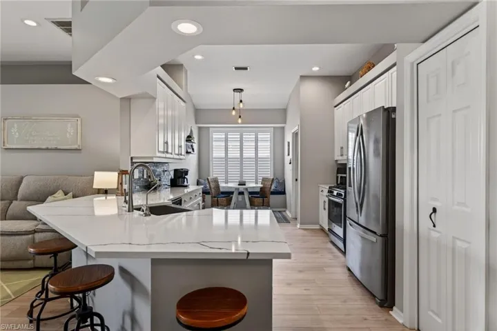 Kitchen with a peninsula, stainless steel appliances, white cabinetry, a breakfast bar area, and light wood-type flooring
