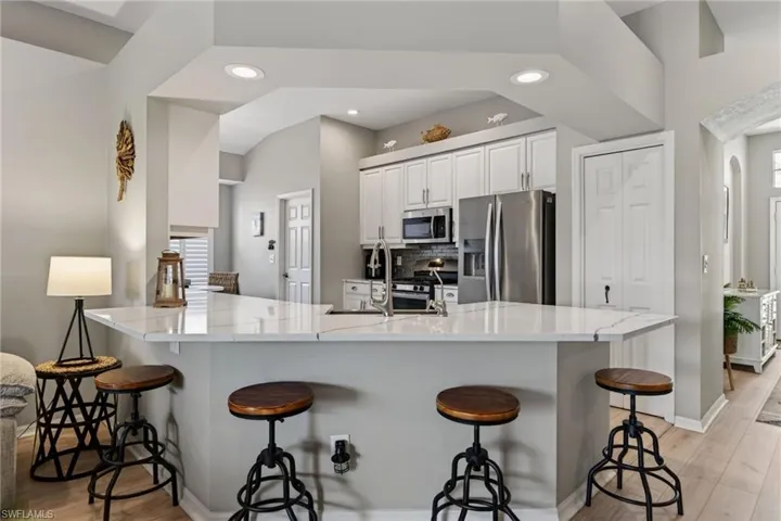 Kitchen with white cabinetry, stainless steel appliances, a breakfast bar area, a peninsula, and recessed lighting