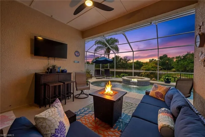 View of patio / terrace with a sunroom, an outdoor lounge area with bar, a lanai, a pool with connected hot tub, and a ceiling fan