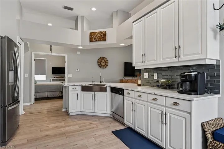 Kitchen featuring stainless steel appliances, a high ceiling, white cabinets, light stone counters, and light wood-style flooring
