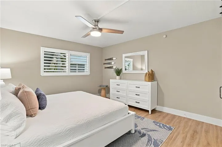 Wood-finish flooring, white plantation shutters, and a central ceiling fan with integrated lighting