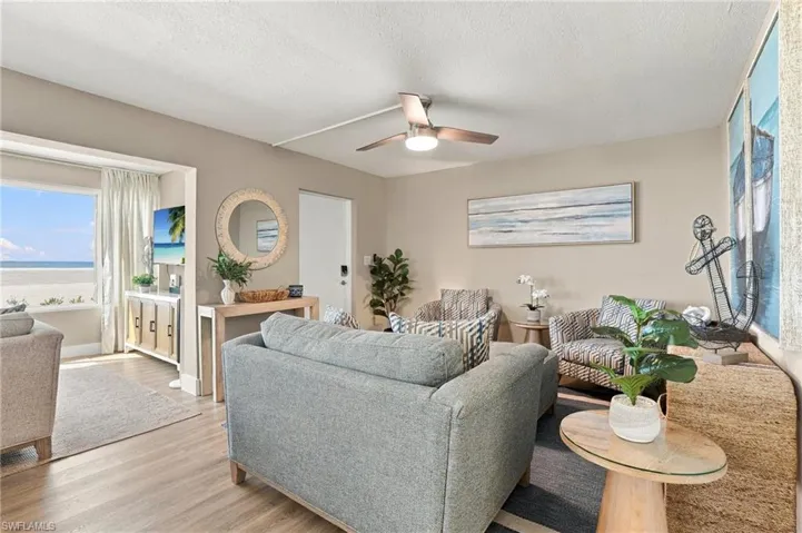 Living area featuring light wood-finish flooring, a ceiling-mounted light fixture with fan blades, and a large window with direct exposure to the beach exterior