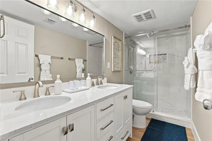 Dual-sink vanity with a quartz countertop, frameless glass shower enclosure, tiled shower surround with an integrated wall niche, and polished metal hardware