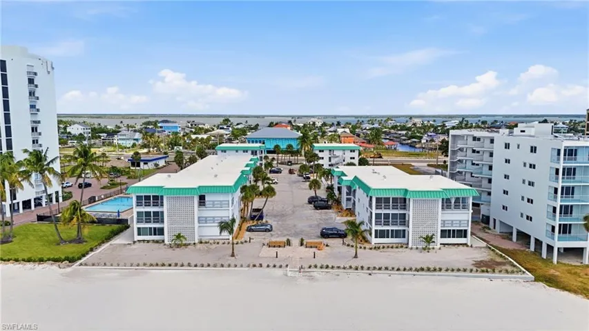 Multi-story residential complex featuring metal roofing, concrete block construction, exterior balconies, and direct coastal access, complemented by an on-site swimming pool