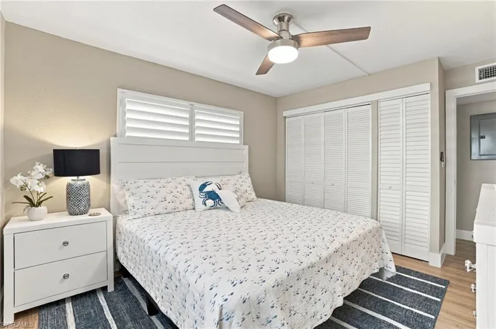 Neutral-toned room featuring a ceiling fan with integrated lighting, wood-finish flooring, horizontal louvered windows, and floor-to-ceiling closets with louvered doors