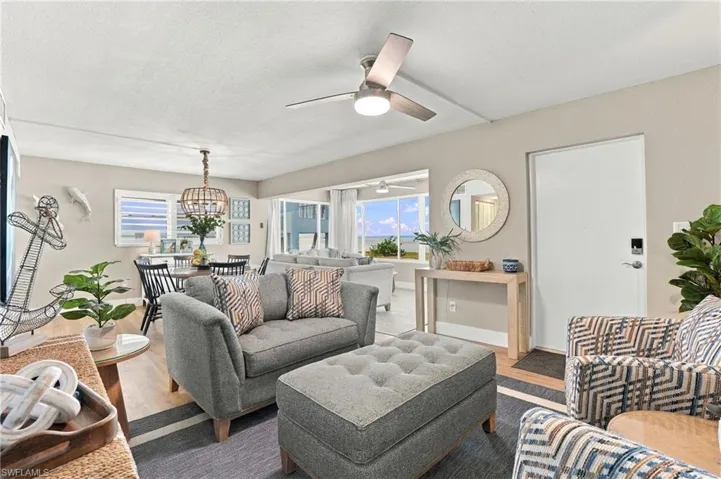 Open-concept living space featuring wood-finish flooring, a contemporary ceiling fan, tiered metal-and-bead chandelier, large-format windows, and a round wall-mounted mirror