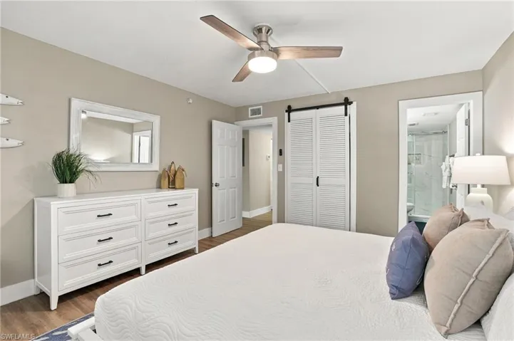 Neutral-toned interior featuring wood-finish flooring, a ceiling fan with integrated lighting, and a white louvered barn door