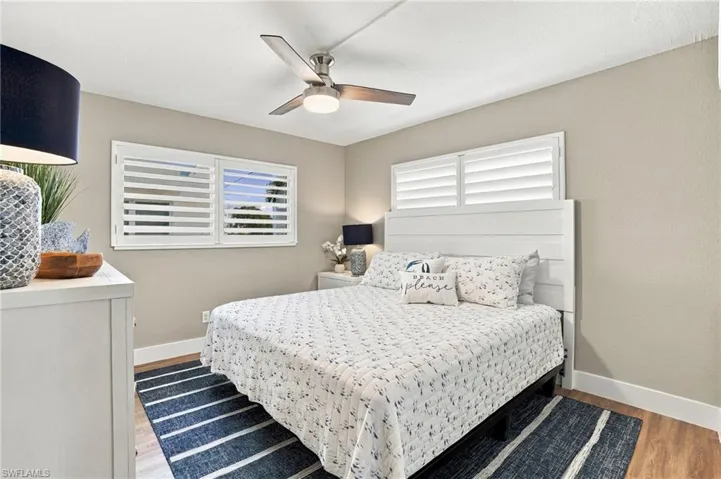 Room featuring wood-finish flooring, white plantation shutters, and a three-blade brushed metal ceiling fan with integrated lighting