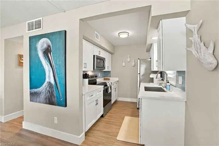 Kitchen featuring white shaker-style cabinetry, solid-surface countertops, wood-finish flooring, stainless steel appliances, and a stainless steel undermount sink