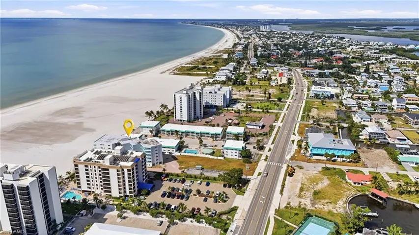 Aerial perspective featuring multi-story residential building, immediate proximity to coastal shoreline, and direct access to expansive sandy beach