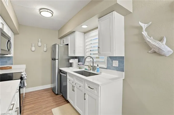 Kitchen featuring white shaker-style cabinetry, solid-surface countertops, blue subway tile backsplash, stainless steel appliances, and wood-finish flooring