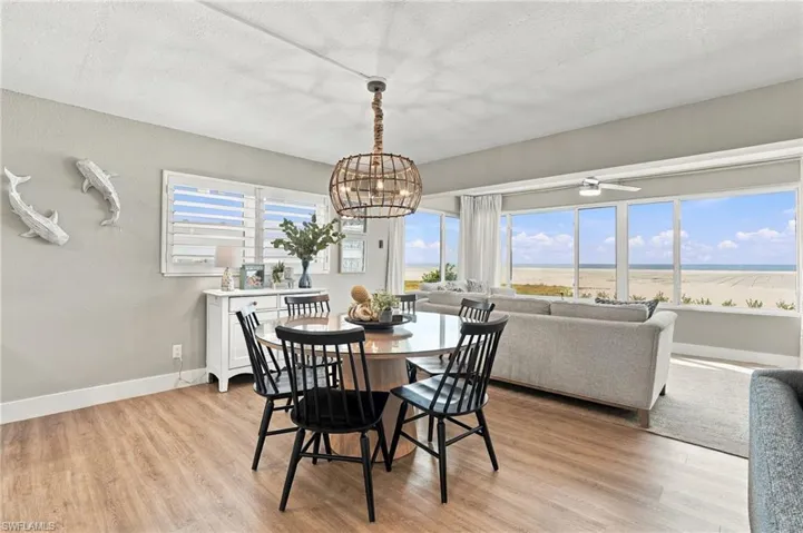 Open-concept living space featuring wood-finish flooring, expansive windows with coastal scenery, and a decorative orb pendant light fixture