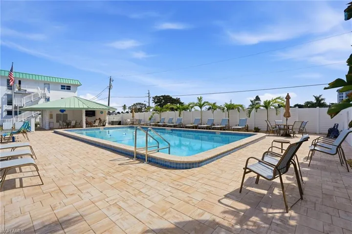 In-ground swimming pool with metal ladder entry, surrounded by a paved patio, covered pavilion, and privacy fencing