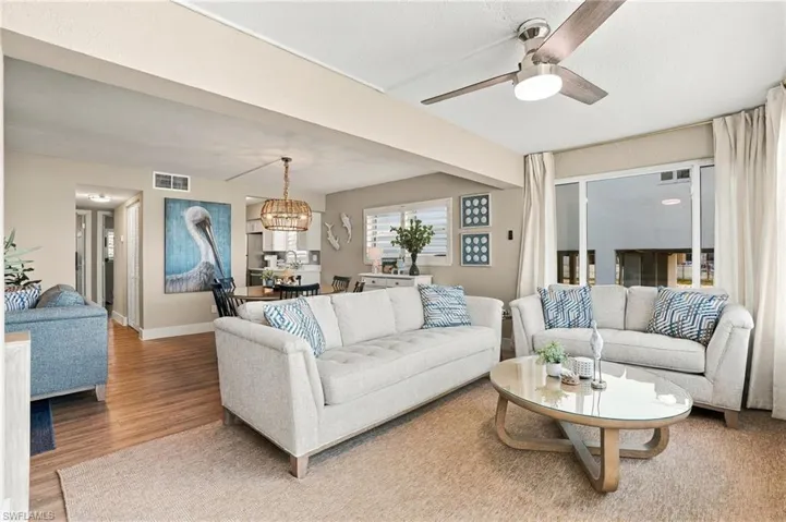 Open-concept living space featuring wood-finish flooring, a ceiling fan with integrated lighting, and large windows with plantation shutters