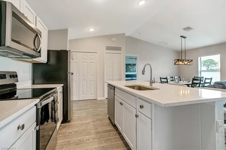 Kitchen with vaulted ceiling, stainless steel appliances, light hardwood / wood-style floors, sink, and a center island with sink