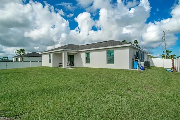 Back of property with cooling unit, a lawn, and a patio