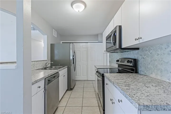 Kitchen featuring white cabinetry, stainless steel appliances, backsplash, sink, and light tile floors