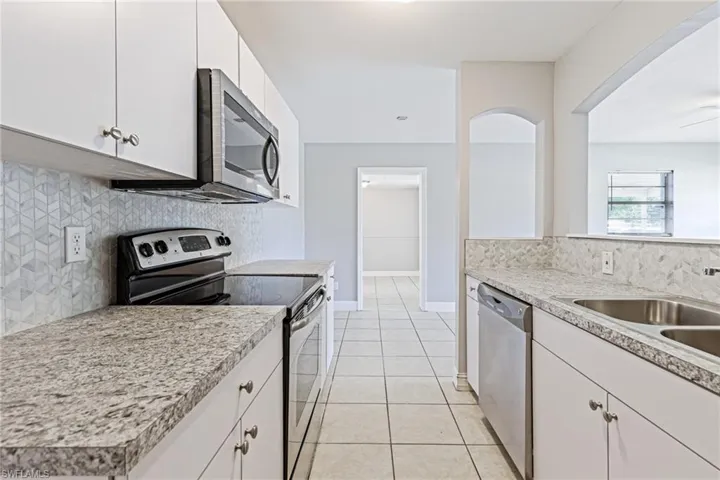 Kitchen with light tile floors, backsplash, white cabinetry, and appliances with stainless steel finishes