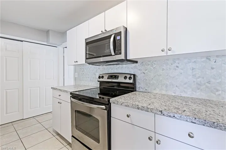 Kitchen with stainless steel appliances, white cabinetry, tasteful backsplash, and light tile floors