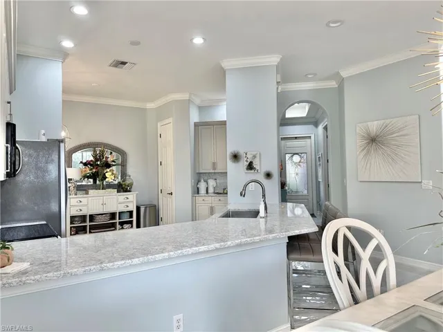 Kitchen featuring sink, decorative backsplash, light stone countertops, crown molding, and black fridge