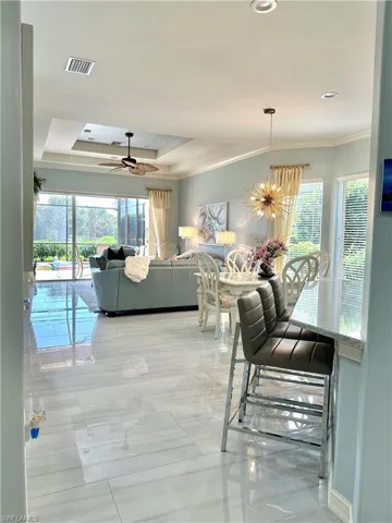 Tiled dining area featuring ceiling fan with notable chandelier, a healthy amount of sunlight, a raised ceiling, and crown molding