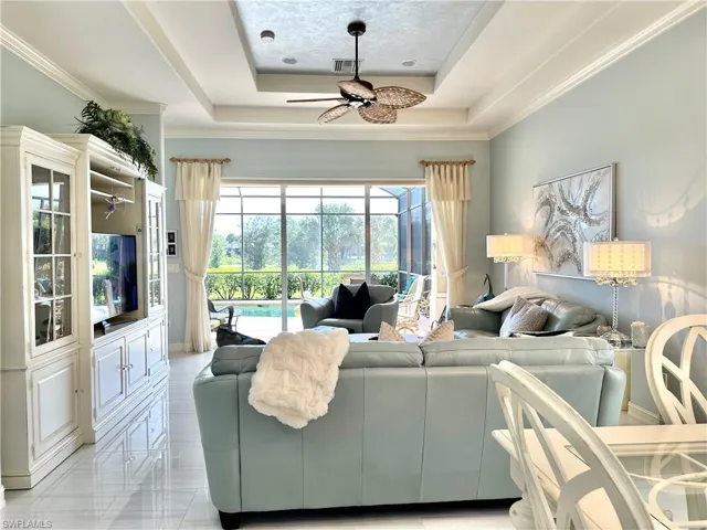 Living room featuring a tray ceiling, crown molding, light tile patterned floors, and ceiling fan