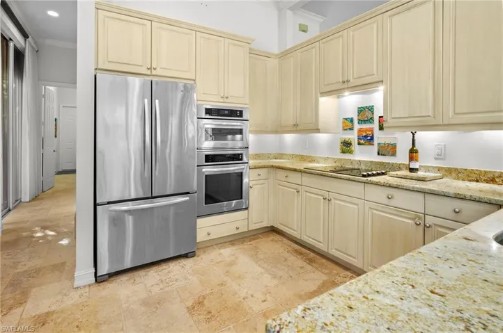Kitchen with stainless steel appliances, light stone countertops, ornamental molding, cream cabinets, and stone tile flooring