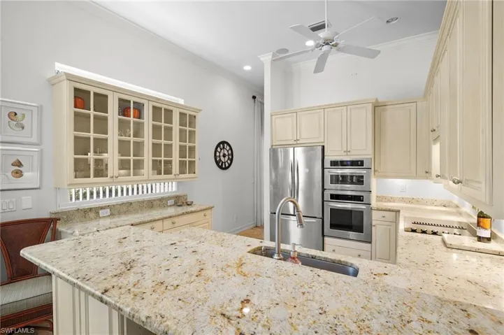 Kitchen with glass fronted cabinets, stainless steel appliances, ornamental molding, cream cabinets, and light stone countertops