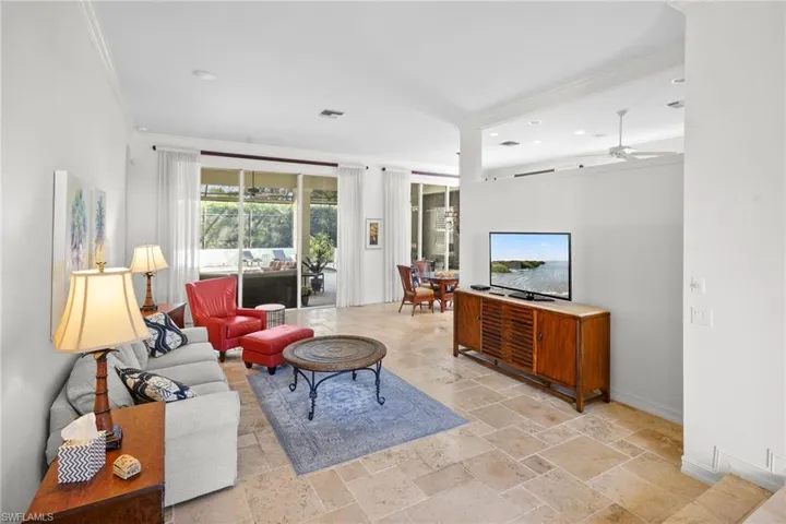 Living area featuring a ceiling fan, stone tile flooring, and ornamental molding