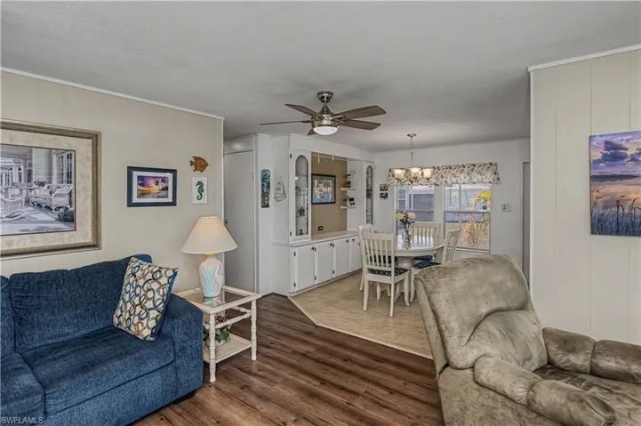 Living area with ceiling fan, hanging lights, wood finished floors, wooden walls, and ornamental molding