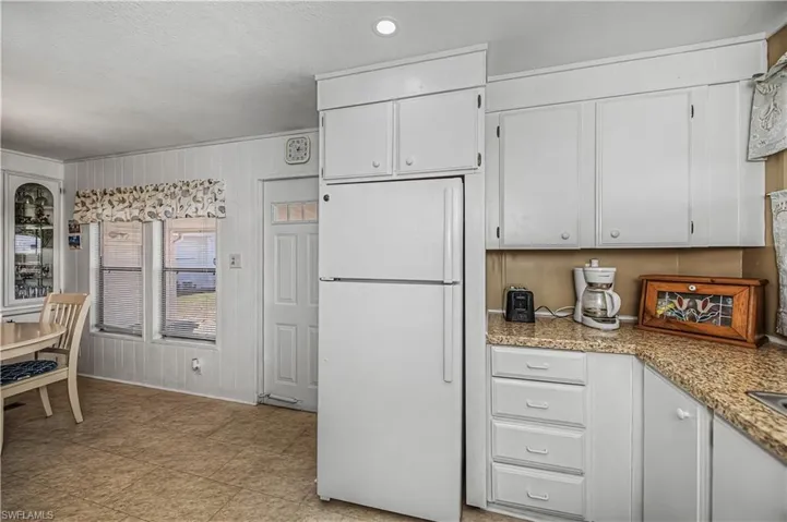 Kitchen featuring white cabinetry, freestanding refrigerator, light stone counters, and a textured ceiling