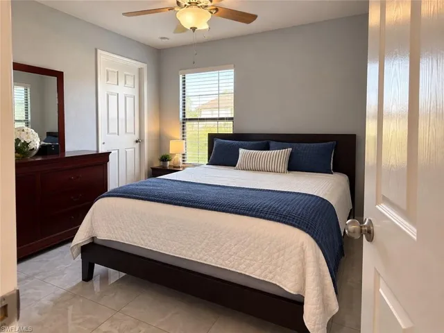 Neutral wall finish, large-format tile flooring, six-panel interior door, and ceiling fan with integrated lighting