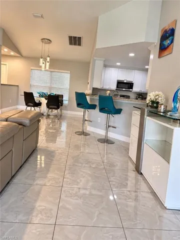 Polished stone-finish tile flooring, vaulted ceilings, breakfast bar with stone-finish countertop, white shaker-style cabinetry, and multi-pendant lighting fixture