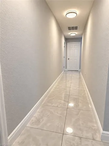 Hallway featuring large-format polished tile flooring, neutral wall paint, and dual flush-mount ceiling light fixtures