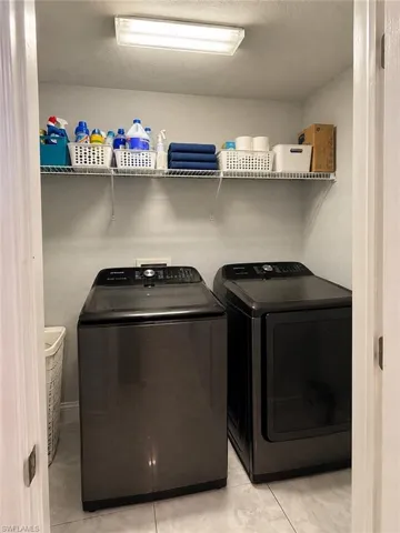 Laundry closet featuring metallic finish top-load washer and dryer, white wire shelving, and neutral floor tile
