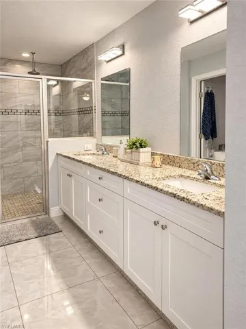 Double vanity featuring white cabinetry, stone-surface countertops, dual rectangular undermount sinks, and wall-mounted light fixtures
