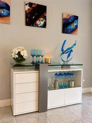 Built-in white storage cabinetry featuring a glass top surface, metallic vertical accents, integrated under-cabinet glassware storage, and mirrored interior backing